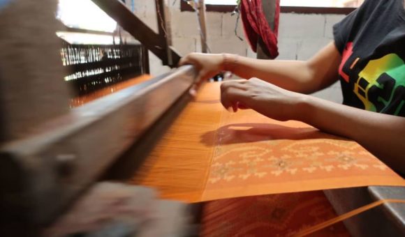 A weaver working on a new orange textile using a traditional loom.